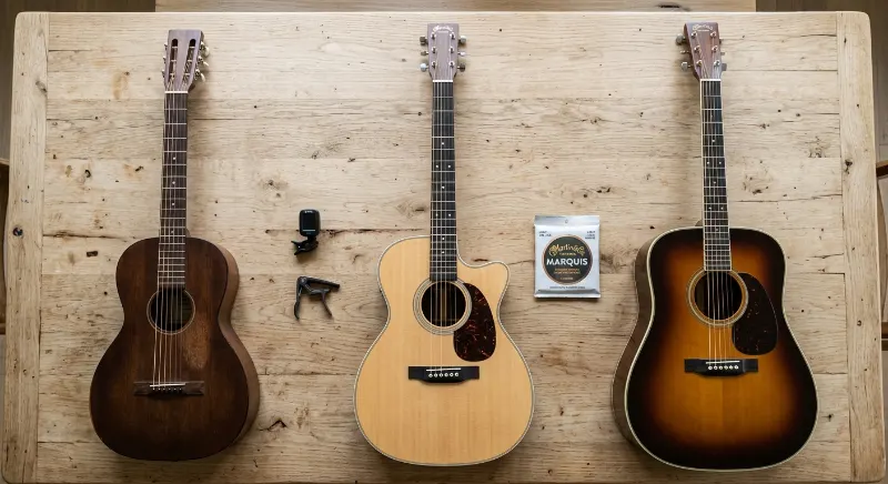 Trois guitares folk de differents formats et budgets posees cote a cote avec accessoires — accordeur, capo et jeu de cordes